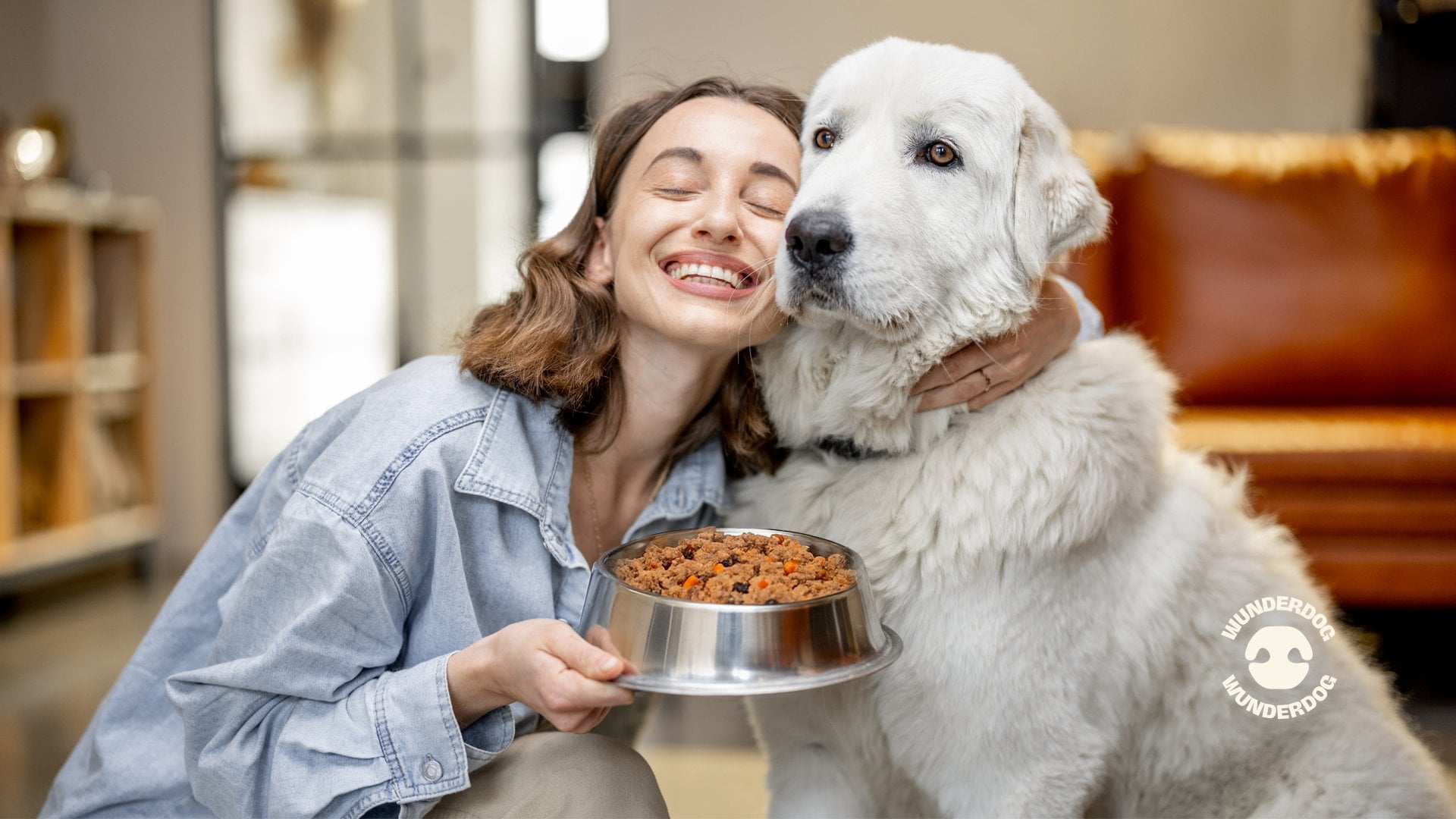 Happy woman hugging her large white dog while holding a bowl of Wunderdog fresh dog food, showcasing the bond between pets and healthy nutrition at home.